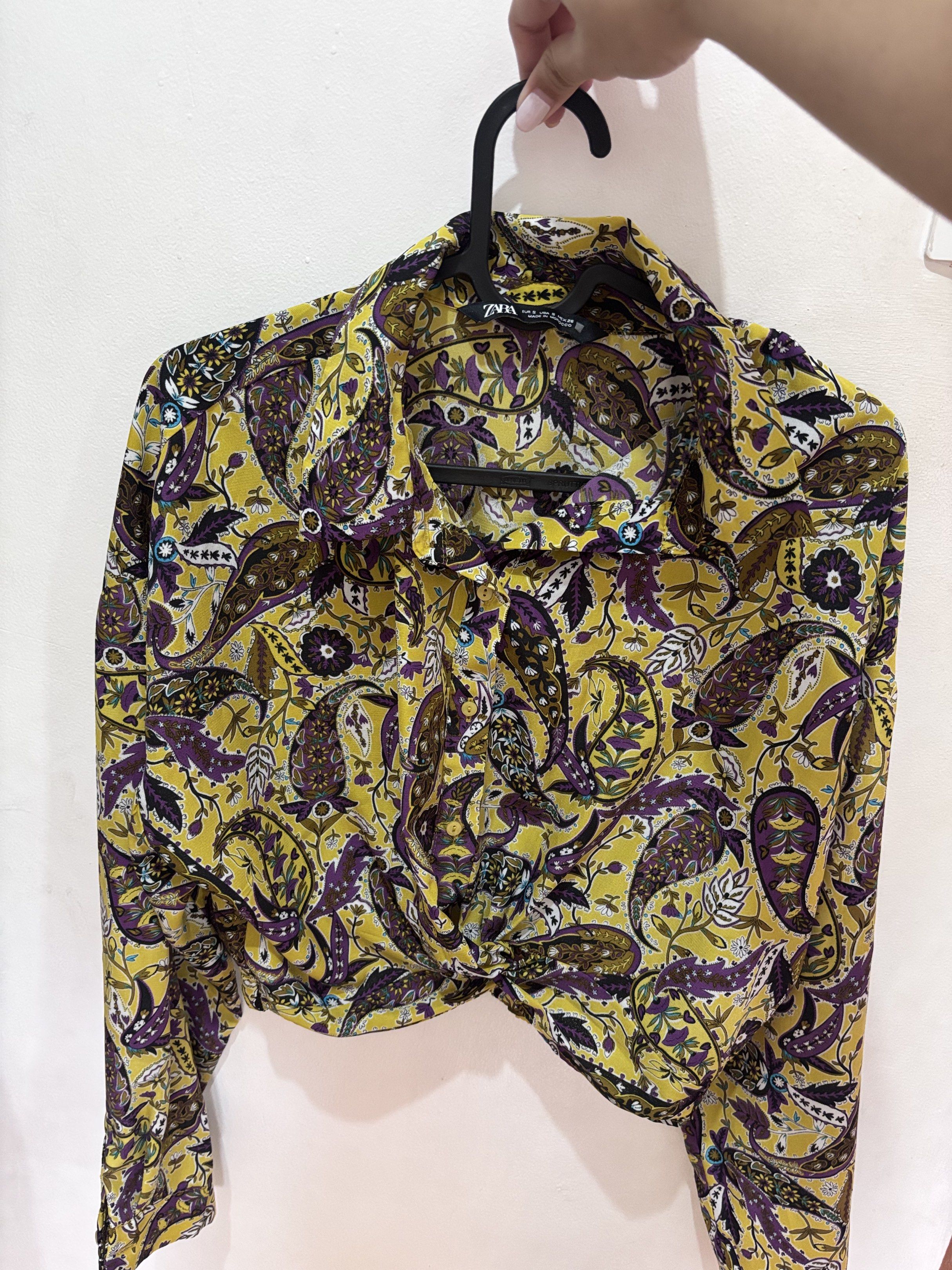 Zara Paisley Print Cropped Blouse (Category: Blouses) located in Meycauayan. Submitted by declutter0403 (Listing ID 1418817159, Image 1). Description: - Zara paisley blouse - Vibrant yellow and purple print - Cropped, knotted style - Size S - Long sleeves - Collared neckline - Button-down closure - Elastic hem at the back.
