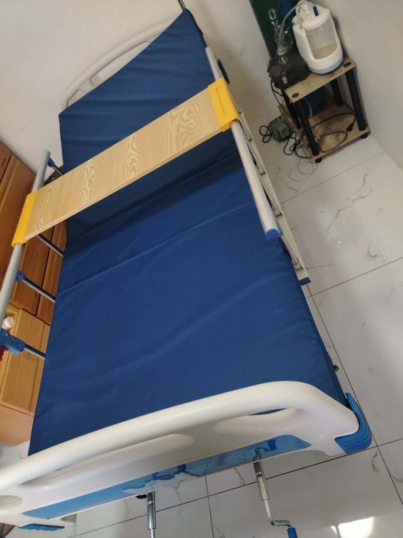 Adjustable Hospital Bed with Side Rails (Category: Medical Supplies & Tools) located in Manila. Submitted by rmpahayaha40866 (Listing ID 1413554245, Image 2). Description: Adjustable hospital bed with blue mattress and side rails. Features a wooden tray. The bed frame is white and silver. Includes adjustable head and foot sections. Suitable for home or clinical use..