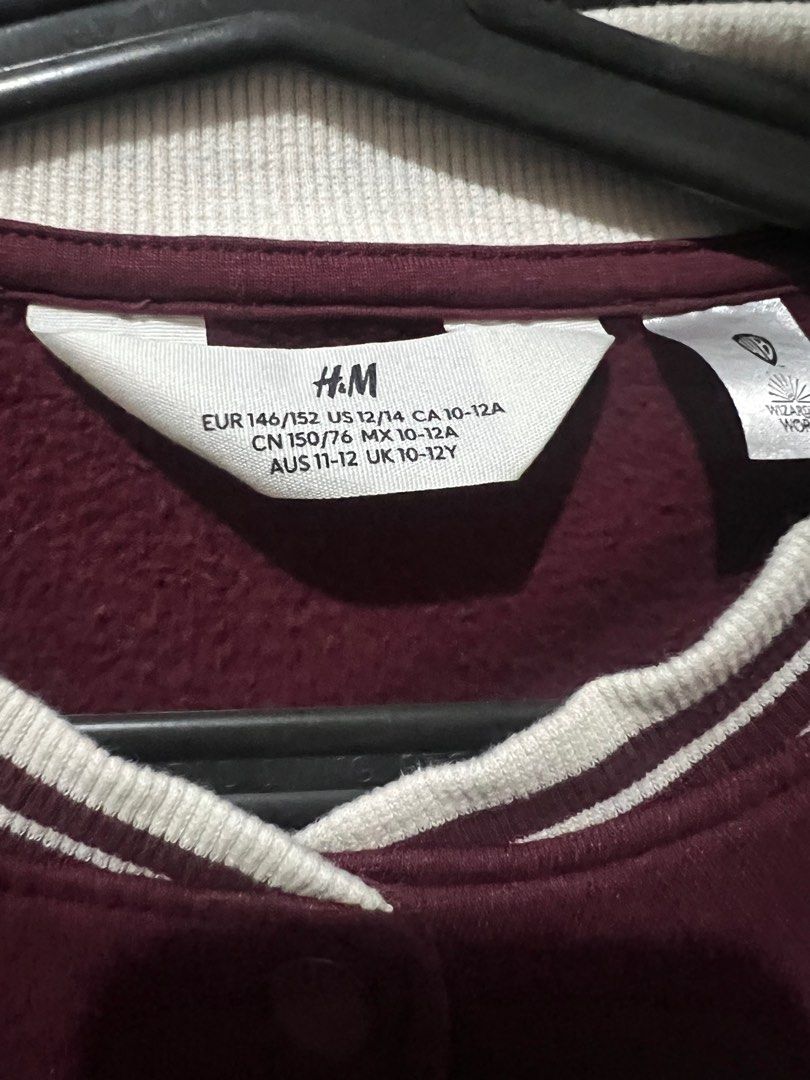 H&M Harry Potter Varsity Jacket (Category: Babies & Kids Fashion) located in San Mateo. Submitted by junked (Listing ID 1413616495, Image 2). Description: Maroon H&M varsity jacket with Harry Potter patches. Features white stripes on the sleeves and a "07" on the back. The jacket has a cropped fit and a button-up front. Size is EUR 146/152, US 12/14, CA 10-12A, CN 150/76, MX 10-12A, AUS 11-12, UK 10-12Y. Some wear and tear is visible on the sleev