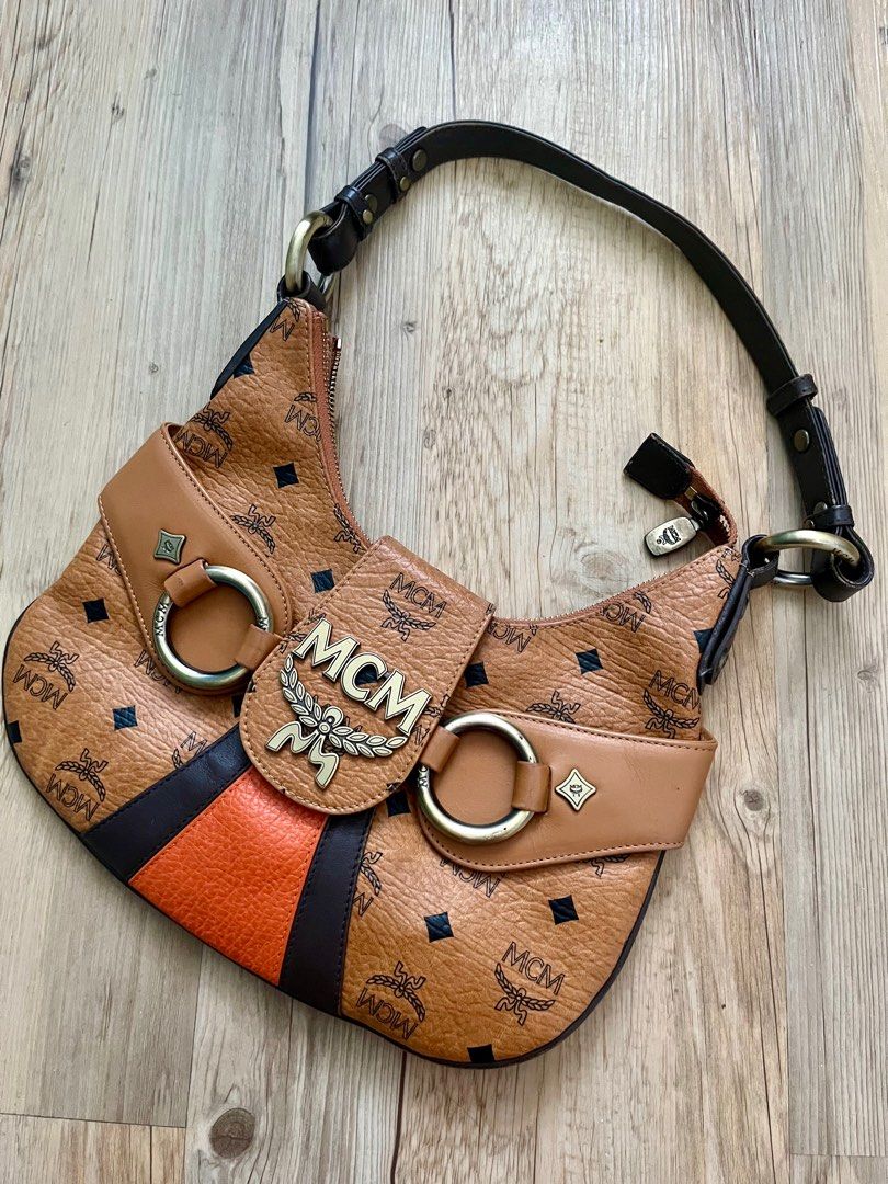MCM Hobo Bag (Category: Luxury Bags & Wallets) located in Taguig. Submitted by norie.m (Listing ID 1413547654, Image 1). Description: - Authentic MCM hobo bag - Iconic MCM logo print - Stylish design with black and orange stripe detail - Top handle - Secure closure - Brown leather exterior - Gold-tone hardware.