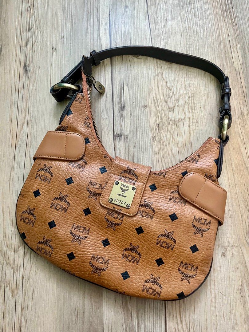MCM Hobo Bag (Category: Luxury Bags & Wallets) located in Taguig. Submitted by norie.m (Listing ID 1413547654, Image 2). Description: - Authentic MCM hobo bag - Iconic MCM logo print - Stylish design with black and orange stripe detail - Top handle - Secure closure - Brown leather exterior - Gold-tone hardware.