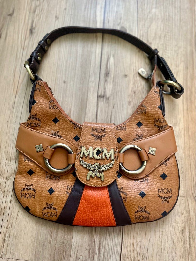 MCM Hobo Bag (Category: Luxury Bags & Wallets) located in Taguig. Submitted by norie.m (Listing ID 1413547654, Image 3). Description: - Authentic MCM hobo bag - Iconic MCM logo print - Stylish design with black and orange stripe detail - Top handle - Secure closure - Brown leather exterior - Gold-tone hardware.