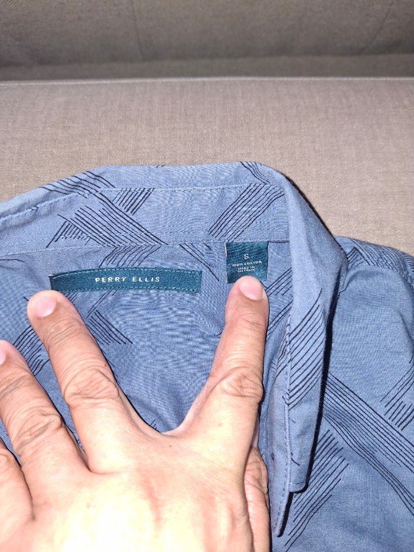 Perry Ellis Short Sleeve Shirt (Category: Tshirts & Polo Shirts ) located in Muntinlupa City. Submitted by eiramceegee (Listing ID 1413525350, Image 2). Description: Blue short sleeve shirt from Perry Ellis. Features a button-down front and a unique pattern. The shirt has a collar and short sleeves. The size is indicated as S. Made from a lightweight fabric, suitable for casual wear. Perfect for everyday use..