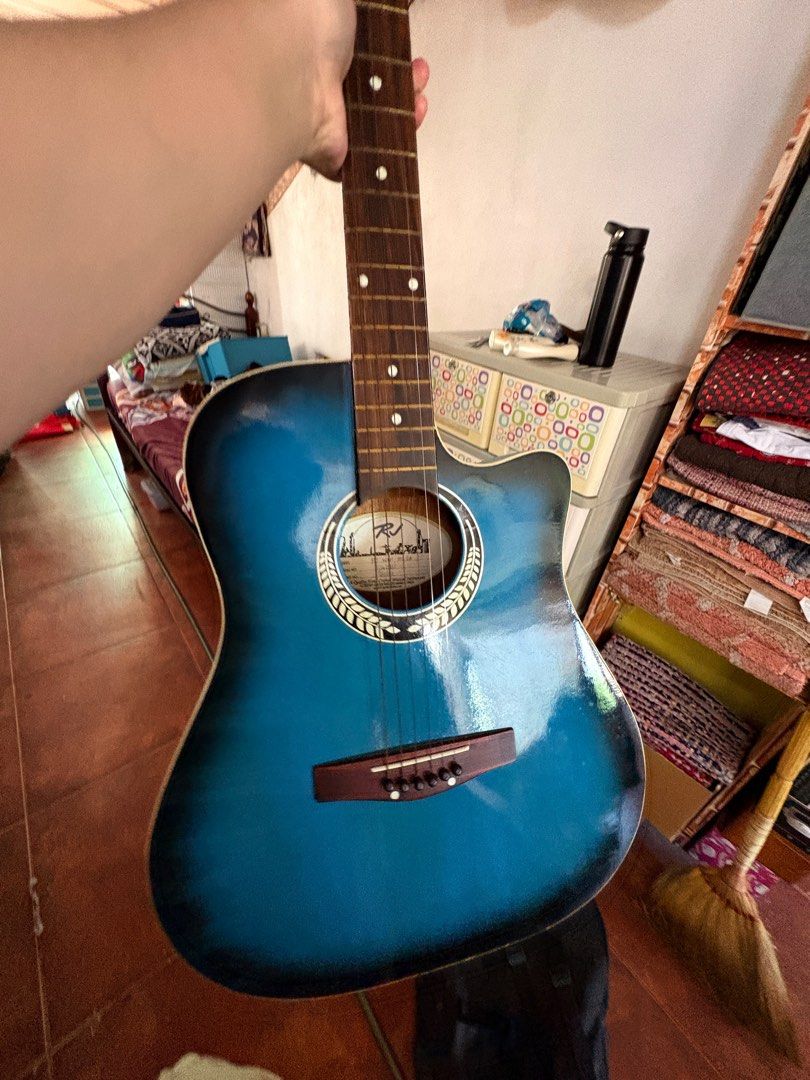 RJ Blue Acoustic Guitar (Category: Musical Instruments) located in Pasig City. Submitted by ddeulgikom (Listing ID 1413495521, Image 2). Description: - RJ acoustic guitar with blue finish. - Cutaway design for easy access to higher frets. - Features a wooden bridge and rosette around the soundhole. - Blue headstock with white tuning pegs. - Comes with a black bag. RFS: No time to learn.