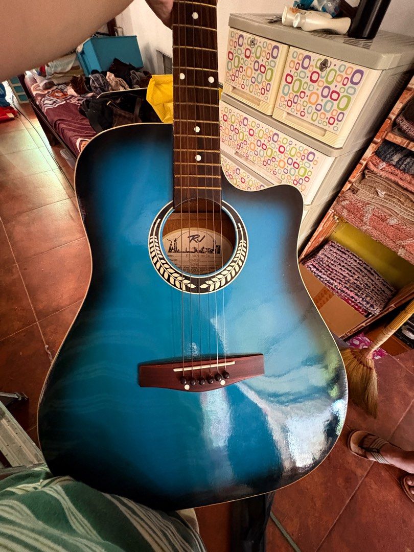 RJ Blue Acoustic Guitar (Category: Musical Instruments) located in Pasig City. Submitted by ddeulgikom (Listing ID 1413495521, Image 3). Description: - RJ acoustic guitar with blue finish. - Cutaway design for easy access to higher frets. - Features a wooden bridge and rosette around the soundhole. - Blue headstock with white tuning pegs. - Comes with a black bag. RFS: No time to learn.