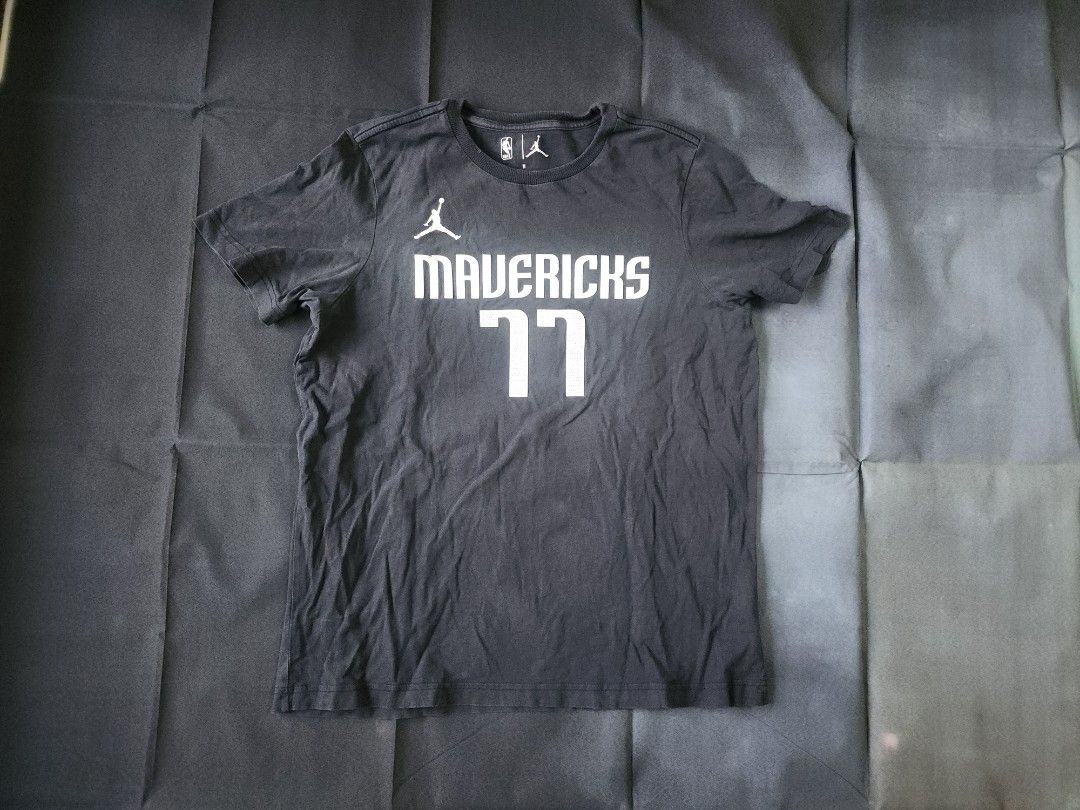 Mavericks luca Doncic 77 T-shirt (Category: Tshirts & Polo Shirts ) located in Manila. Submitted by cardano (Listing ID 1413843103, Image 1). Description: Black Jordan T-shirt featuring the Mavericks logo and Doncic's number 77. The shirt has a crew neck and the NBA logo is visible. The size is M. The shirt has some minor imperfections, including a small hole near the collar. The back of the shirt displays Doncic's name and number..