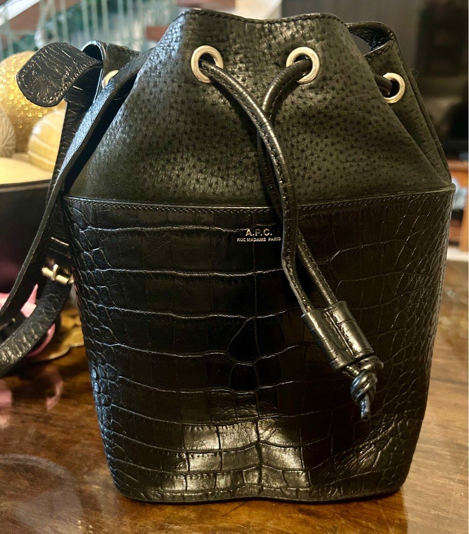 A.P.C. Black Bucket Bag (Category: Luxury Bags & Wallets) located in Quezon City. Submitted by asiaco (Listing ID 1413912430, Image 1). Description: Black bucket bag from A.P.C. Features a drawstring closure and a shoulder strap. The bag has a textured upper section and a crocodile-embossed lower section. The interior includes a zippered pocket. A.P.C. logo is visible on the front of the bag. Very nice. .
