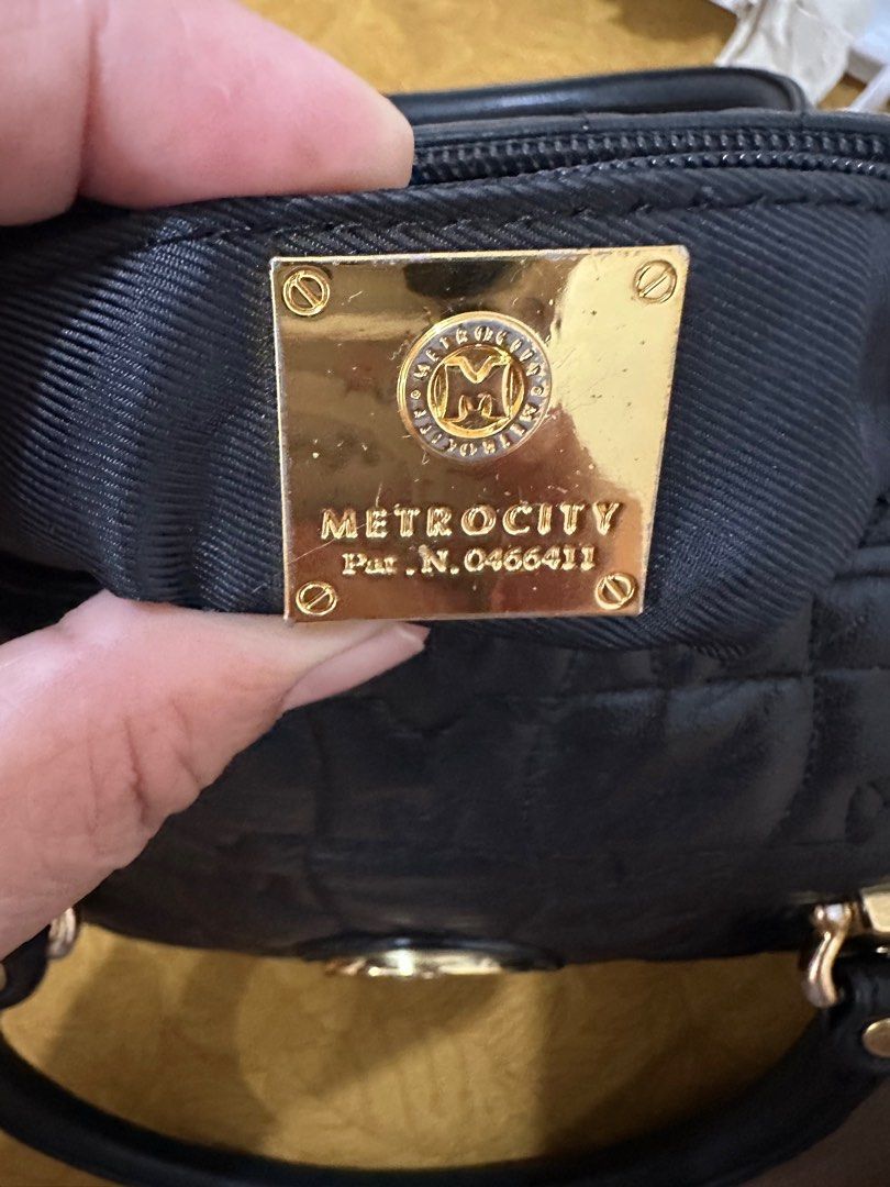 Metrocity Black Handbag (Category: Luxury Bags & Wallets) located in Antipolo. Submitted by jlonline_1207 (Listing ID 1414035937, Image 3). Description: Black Metrocity handbag with gold-tone hardware. Features a quilted design with the Metrocity logo prominently displayed. Includes a top handle and a detachable tassel. The bag has a zip closure and gold accents on the corners. The interior lining is black. Now sale.
