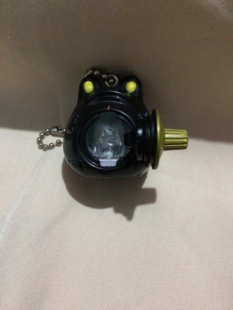 Bandai 2002 Frog Keychain (Category: Character Goods) located in Baguio. Submitted by green.attic (Listing ID 1414159887, Image 2). Description: - Vintage Bandai frog keychain - Released in 2002 - Features a black frog design - Yellow eyes and gold-colored dial - Includes a ball chain - Has a small, opening compartment - Marked "B. China" on the bottom.