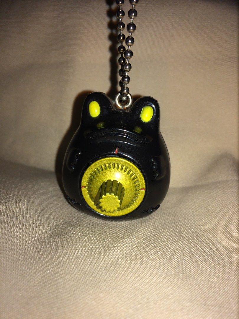 Bandai 2002 Frog Keychain (Category: Character Goods) located in Baguio. Submitted by green.attic (Listing ID 1414159887, Image 1). Description: - Vintage Bandai frog keychain - Released in 2002 - Features a black frog design - Yellow eyes and gold-colored dial - Includes a ball chain - Has a small, opening compartment - Marked "B. China" on the bottom.