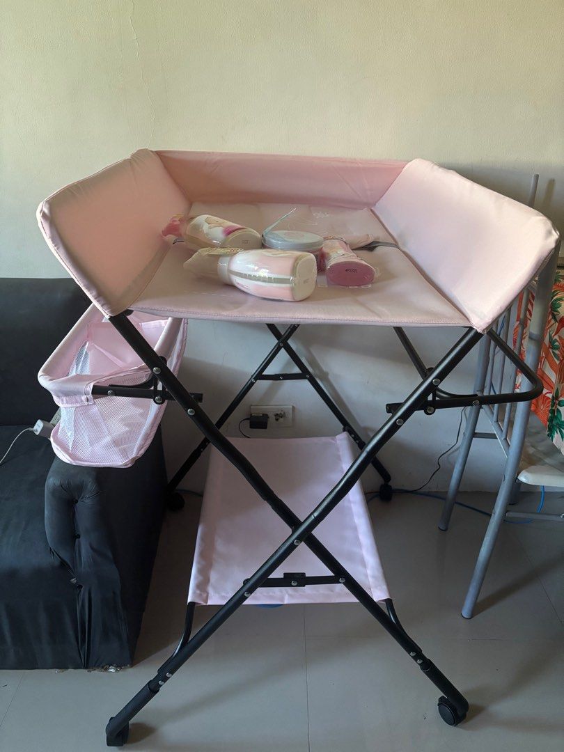 Foldable Baby Changing Table (Category: Changing Mats & Accessories) located in Binan City. Submitted by gracefully714 (Listing ID 1414300048, Image 1). Description: - Foldable baby changing table - Pink changing surface - Black metal frame - Side storage basket - Lower storage shelf - Wheels for easy movement - Includes baby care products.