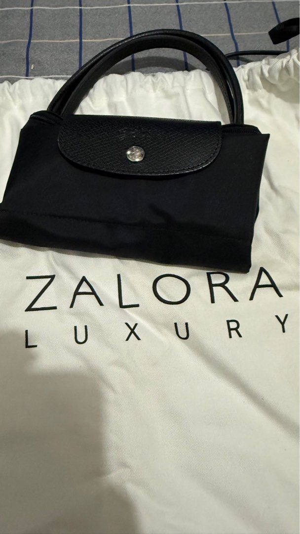 Longchamp Le Pliage Handbag (Category: Luxury Bags & Wallets) located in Quezon City. Submitted by pattyeval (Listing ID 1414253408, Image 1). Description: - Black Longchamp Le Pliage handbag - Flap closure with button - Leather handles - Zipper closure with Longchamp logo charm - Spacious interior - Includes Zalora Luxury dust bag and box - Can provide proof of purchase.