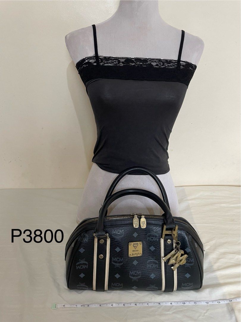 MCM Boston Bag (Category: Luxury Bags & Wallets) located in Tanauan. Submitted by airese (Listing ID 1414623347, Image 2). Description: Black MCM Boston bag with the brand's logo pattern. Features dual top handles, a zip closure, and a metal logo plate. Includes a detachable charm. The bag has a black interior with multiple compartments. The hardware shows some signs of wear. The bag has a beige stripe detail on the front and back..