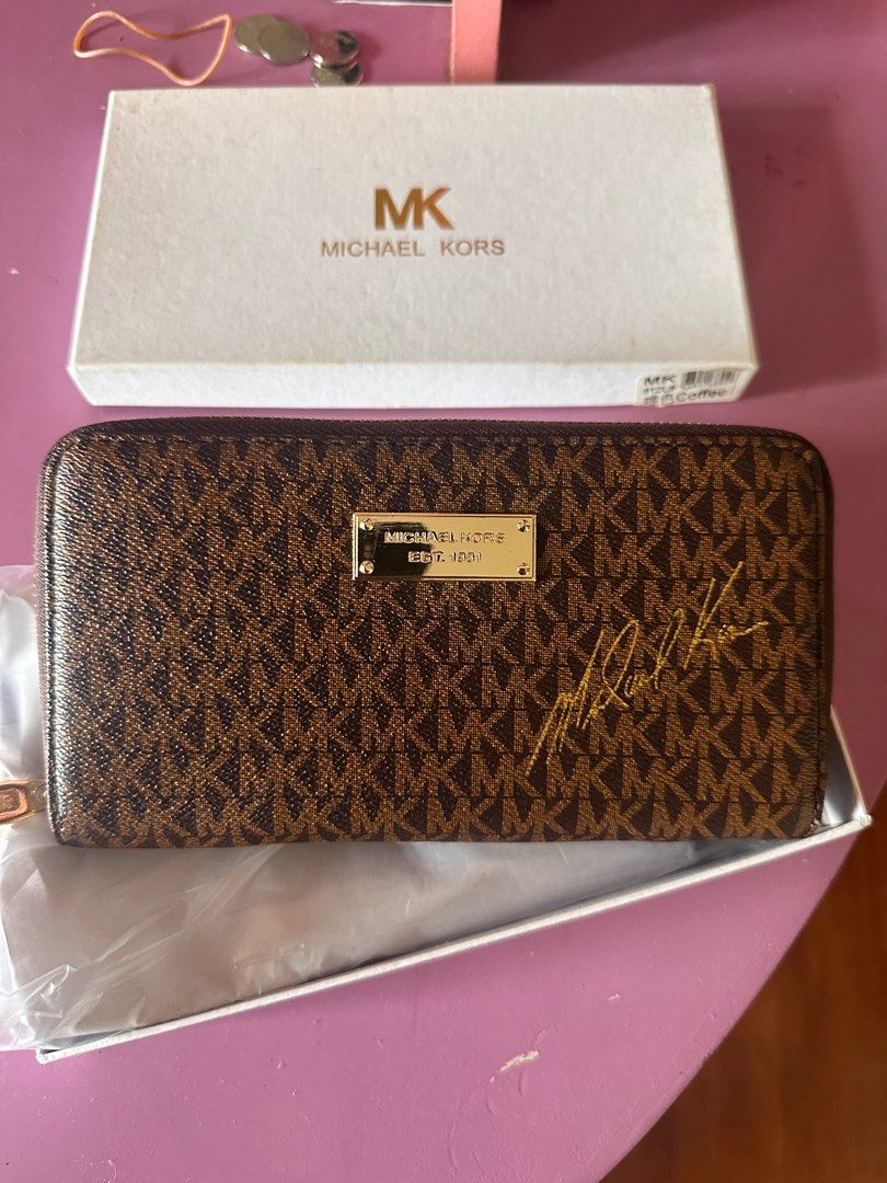 Michael Kors Zip Around Wallet (Class A) (Category: Wallets & Card holders) located in Tanza. Submitted by euniceericka (Listing ID 1414467296, Image 1). Description: - Authentic Michael Kors zip-around wallet (Class A) - Brown with iconic MK logo print - Multiple card slots - Zippered compartment - Gold-tone zipper and hardware - Interior: Orange - Includes original box - Signature detail on front - Never been used RFS: Decluttering .