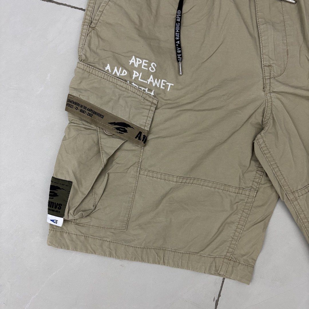Aape By A Bathing Ape Cargo Shorts Beige (Category: Shorts) located in Cavite. Submitted by mana__ (Listing ID 1465309842, Image 3). Description: - Brand: Aape by A Bathing Ape - Color: Beige - Style: Cargo shorts with utility pockets and branded drawstrings - Details: Embroidered 'Apes and Planet' lettering on the right leg, branded tape accents, and circular logo patch - Medium Waist - 31-34 Length - 21 Inseam - 9 Leg op - 12.3 Excellent *Stain