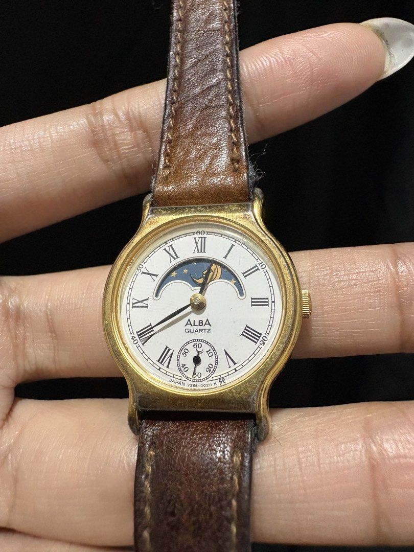 Moonphase Watch Seiko Alba (Category: Men's Watches) located in Caloocan City. Submitted by esnairahhh (Listing ID 1465378107, Image 2). Description: - Brand: Vintage Alba - Movement: Reliable quartz - Display: White dial with Roman numerals, moonphase at 12 o'clock, and small seconds sub-dial - Aesthetics: Gold-tone case and bezel - Condition: Shows visible wear, including cracking on the brown leather strap and fading/tarnishing on the gold pla