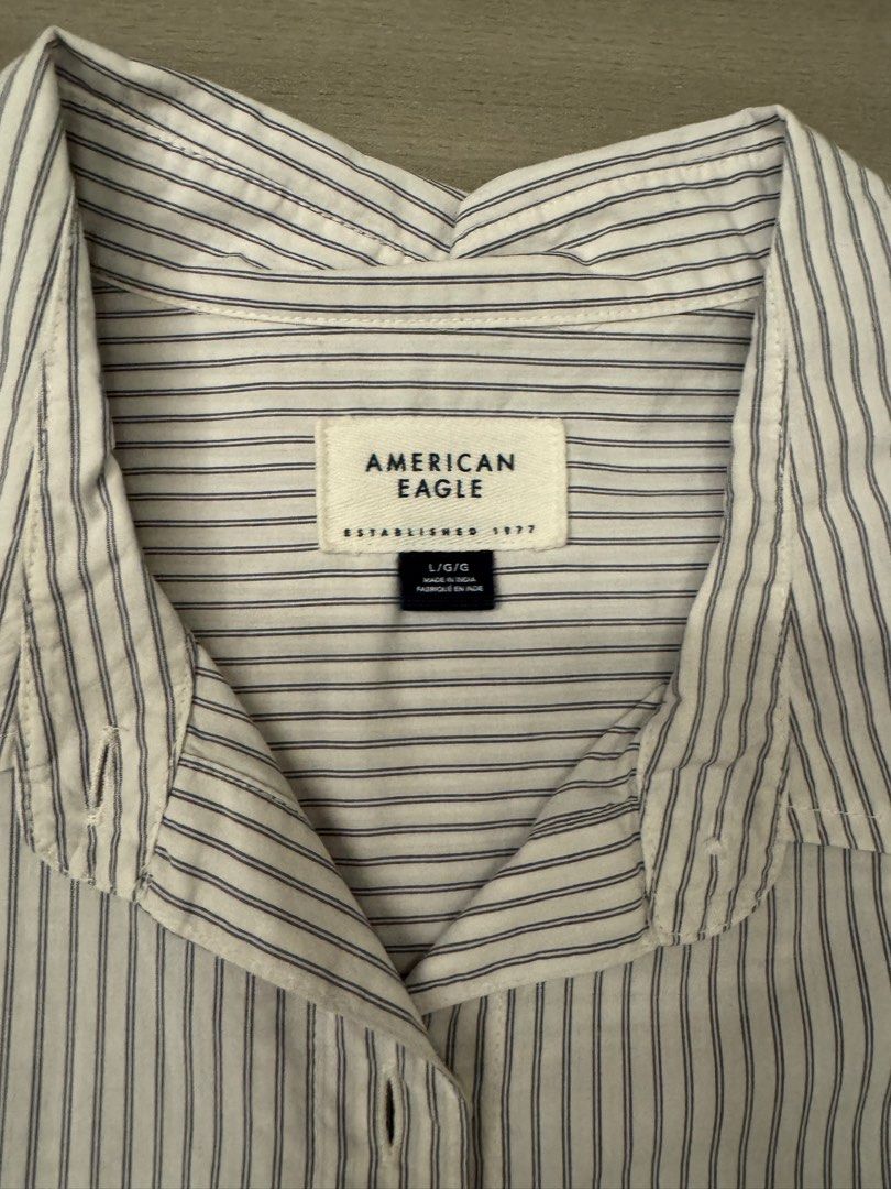 American Eagle Striped Button-Up Long Sleeve Shirt (Category: Longsleeves) located in Taguig. Submitted by sqaumejada (Listing ID 1465288651, Image 2). Description: - Brand: American Eagle - Size: Large - Design: White with navy blue vertical stripes - Features: Front chest pocket, button cuffs, curved hemline, and back pleat detail - Fit: Relaxed fit.