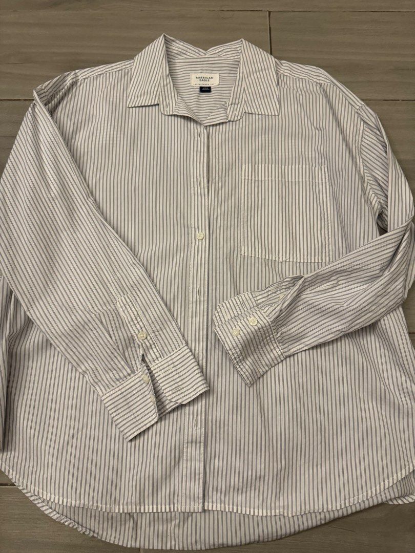 American Eagle Striped Button-Up Long Sleeve Shirt (Category: Longsleeves) located in Taguig. Submitted by sqaumejada (Listing ID 1465288651, Image 1). Description: - Brand: American Eagle - Size: Large - Design: White with navy blue vertical stripes - Features: Front chest pocket, button cuffs, curved hemline, and back pleat detail - Fit: Relaxed fit.