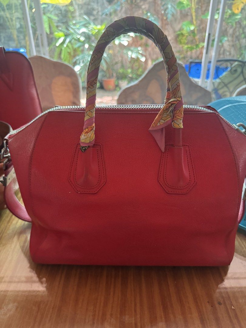Authentic Givenchy Red Leather Handbag with Twilly Scarf (Category: Luxury Bags & Wallets) located in Taguig. Submitted by mhay.molina (Listing ID 1465268055, Image 2). Description: - Brand: Givenchy - Color: Bright red with silver-tone hardware - Material: Premium leather with beige fabric interior - Design: Structured trapezoid shape with embossed logo and protective feet - Handles: Double top handles wrapped in a chic patterned silk twilly sca