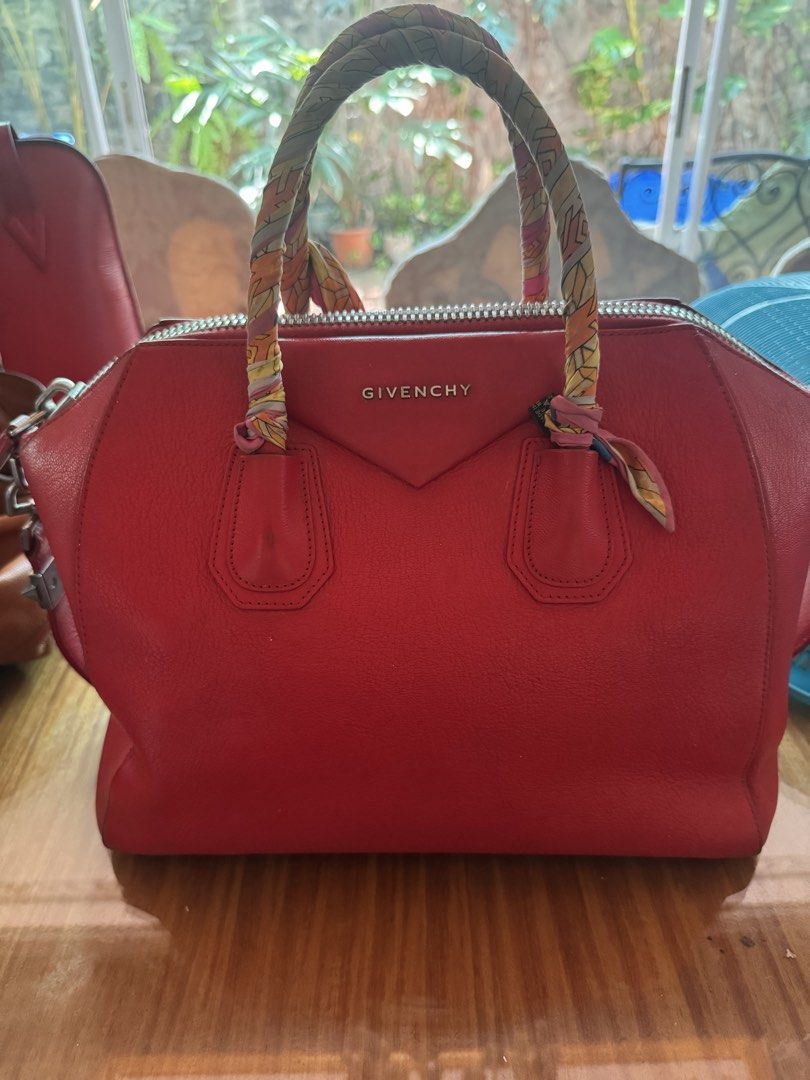 Authentic Givenchy Red Leather Handbag with Twilly Scarf (Category: Luxury Bags & Wallets) located in Taguig. Submitted by mhay.molina (Listing ID 1465268055, Image 1). Description: - Brand: Givenchy - Color: Bright red with silver-tone hardware - Material: Premium leather with beige fabric interior - Design: Structured trapezoid shape with embossed logo and protective feet - Handles: Double top handles wrapped in a chic patterned silk twilly sca