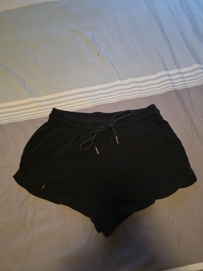 Black cotton drawstring shorts (Category: Shorts) located in Manila. Submitted by cher0918 (Listing ID 1465262775, Image 1). Description: - Color: Black - Material: Soft cotton fabric - Fit: Relaxed, short cut - Waistband: Elasticated with adjustable drawstring and metal tips - Condition: Good, with a small orange stain near the bottom front hem - Style: Basic everyday loungewear.