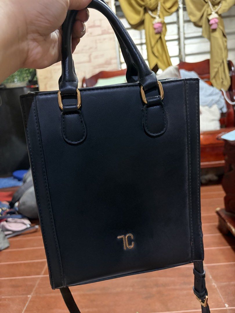 Black structured handbag with top handles and gold hardware (Category: Luxury Bags & Wallets) located in Manila. Submitted by lynnalec25 (Listing ID 1465363225, Image 1). Description: - Sleek vertical rectangular design in classic black - Premium faux leather with neat edge stitching - Dual top handles featuring stylish gold rectangular rings - Elegant gold TC monogram logo stamped on the front - Includes a convenient detachable shoulder strap - 