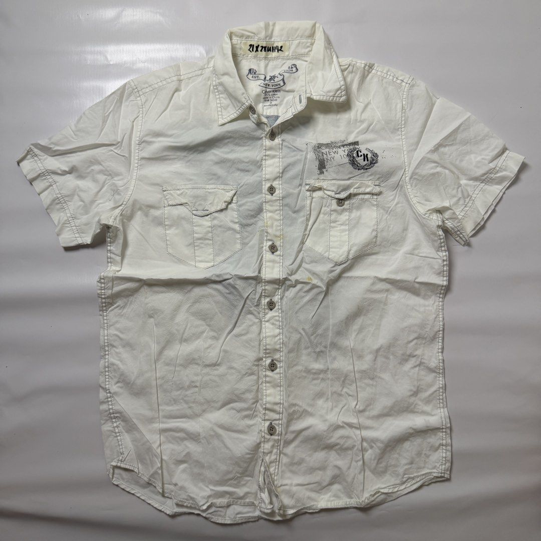 Calvin Klein Graphic Short Sleeve Button Down Shirt White Medium (Category: Tshirts & Polo Shirts ) located in Manila. Submitted by johnedel_james (Listing ID 1465280906, Image 1). Description: - Brand: Calvin Klein - Size: Medium (Modern Fit) - Material: 100% Cotton - Color: White - Details: Short sleeve, branded buttons, dual chest pockets with button flaps, small chest logo, and a bold graphic print on the back - Condition: Excellent, pre-love