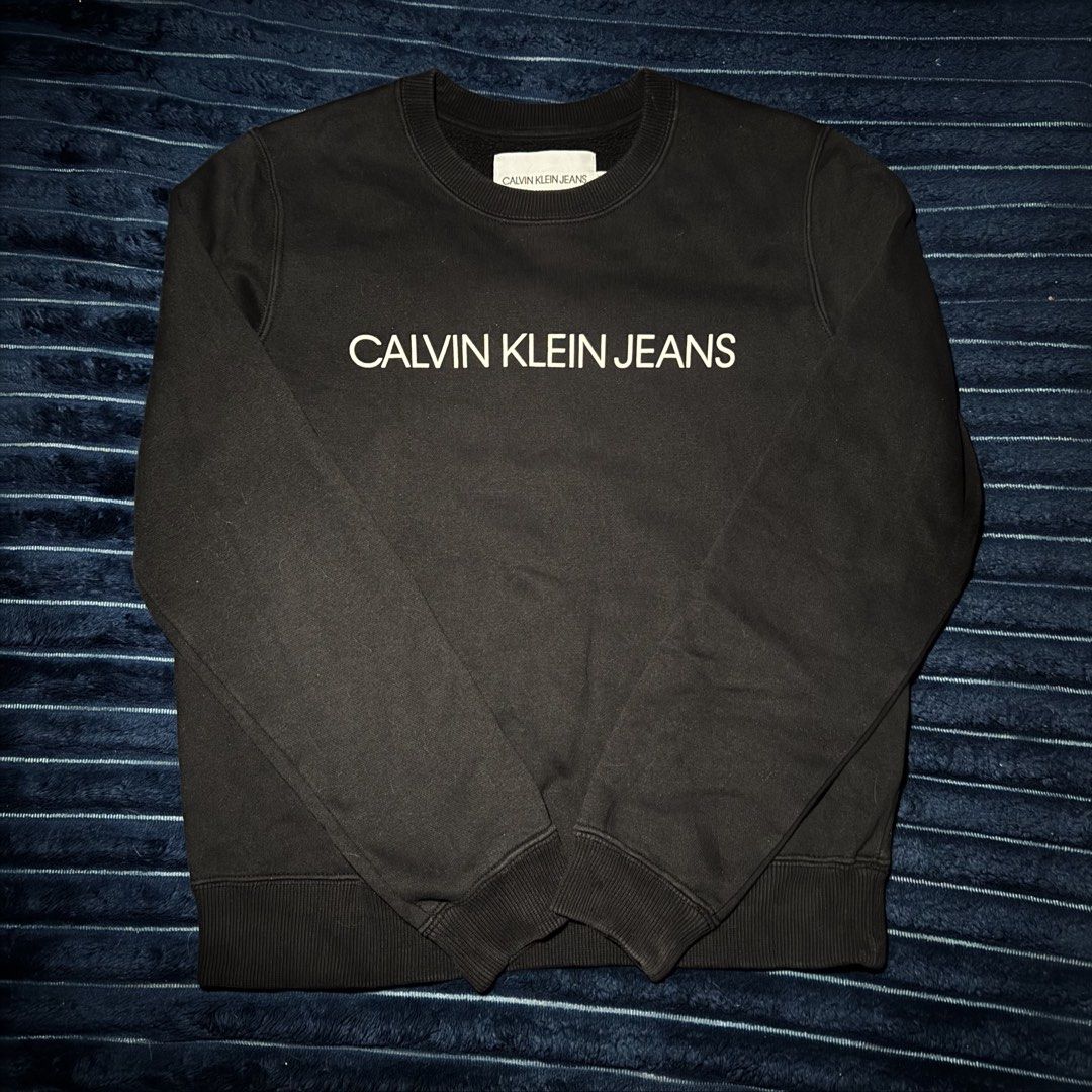 Calvin Klein Jeans Black Sweatshirt (Category: Coats, Jackets and Outerwear) located in San Miguel. Submitted by babycrisreyes (Listing ID 1465300036, Image 1). Description: • Brand: Calvin Klein Jeans • Style: Crewneck Sweatshirt / Pullover • Fit: Unisex (Fits XS to Slim Small) 23x19 • Color: Solid Black • Material: 63% Cotton, 37% Polyester (Soft, breathable & cozy) • Condition: 9/10 (clean print/logo, complete internal wash tags).