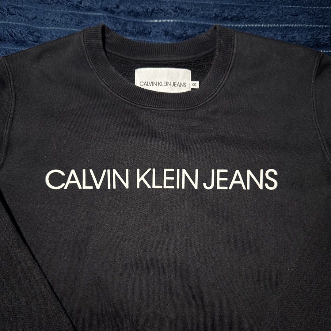 Calvin Klein Jeans Black Sweatshirt (Category: Coats, Jackets and Outerwear) located in San Miguel. Submitted by babycrisreyes (Listing ID 1465300036, Image 2). Description: • Brand: Calvin Klein Jeans • Style: Crewneck Sweatshirt / Pullover • Fit: Unisex (Fits XS to Slim Small) 23x19 • Color: Solid Black • Material: 63% Cotton, 37% Polyester (Soft, breathable & cozy) • Condition: 9/10 (clean print/logo, complete internal wash tags).