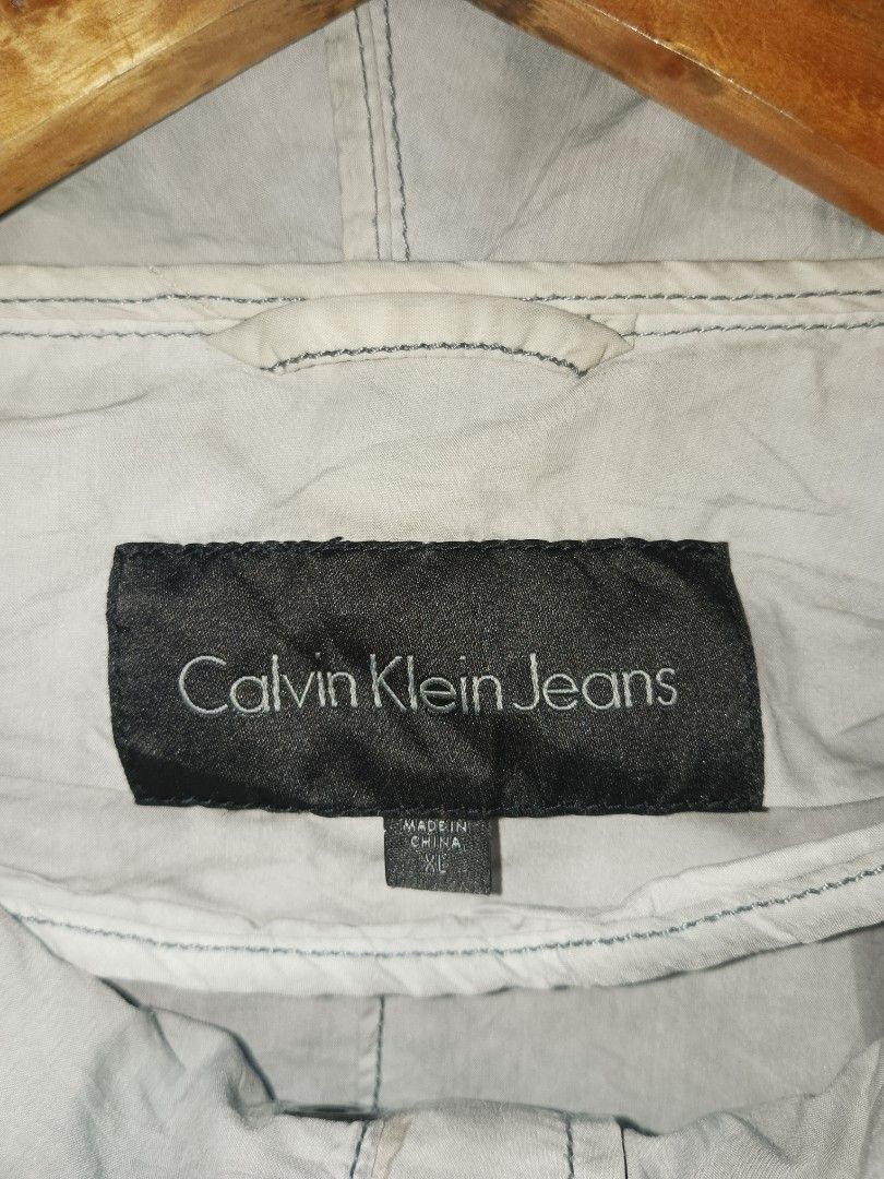 Calvin Klein Jeans Grey Hooded Jacket (Category: Coats, Jackets and Outerwear) located in Jolo. Submitted by zah-zah (Listing ID 1465382159, Image 3). Description: - Brand: Calvin Klein Jeans - Color: Grey - Size: XL - Material: 61% cotton, 39% nylon - Closure: Full front zipper with snap button storm flap - Features: Adjustable hood drawstrings, 2 large front flap pockets, ribbed wrist cuffs, and metal logo plate on sleeve.
