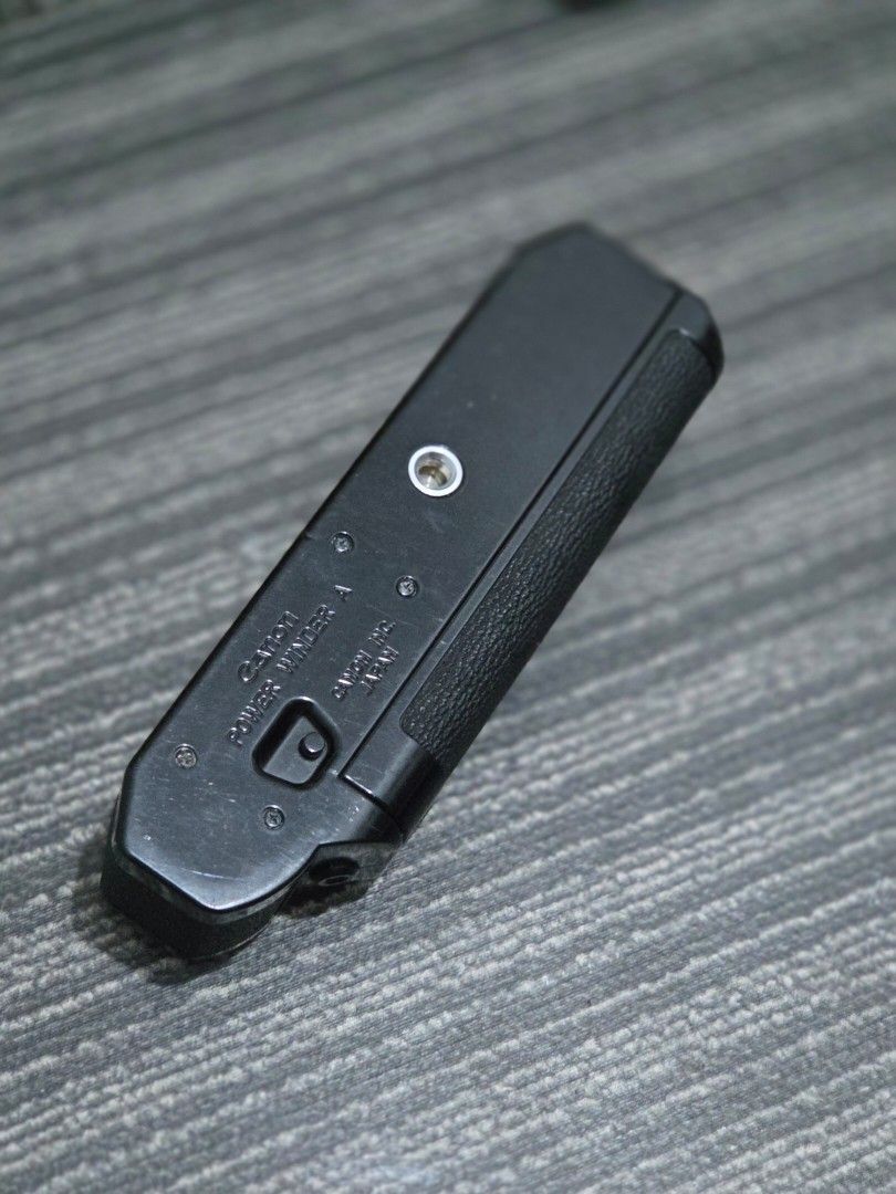 Canon Power Winder A (Category: Cameras) located in Manila. Submitted by manilafilmshop (Listing ID 1465183397, Image 3). Description: Canon Power Winder A for film SLR cameras. Black textured body with standard tripod mount underneath. Battery compartment clean inside, takes AA batteries. Switch on the side controls operation. Tested mechanism works smoothly. Minor scuffs on the outer casing from normal handling over time..