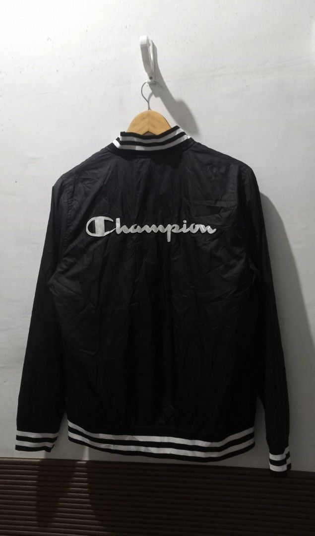 Champion Black Bomber Jacket Size Large (Category: Coats, Jackets and Outerwear) located in Taguig. Submitted by mvdsh0p2022 (Listing ID 1465273895, Image 2). Description: - Brand: Champion - Style: Bomber Jacket - Color: Black with white striped ribbed collar, cuffs, and hem - Size: Large (Tag inside) - Details: Large embroidered Champion logo patch on left chest, big Champion script logo across the back - Interior: Red mesh lining - Closure: Fr