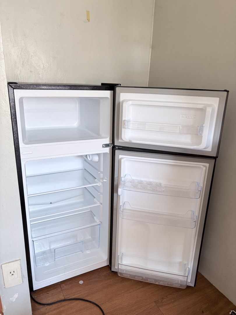 CHiQ Double Door Refrigerator (Category: Refrigerators and Freezers) located in Pasig City. Submitted by petite_declutter (Listing ID 1465377617, Image 3). Description: Dark grey finish, dual door setup. Top freezer, bottom fridge with adjustable wire shelves and clear door bins. Includes crisper drawer at the bottom. Standard two-prong plug. Clean interior, ready for use. Dimensions suit a compact kitchen or dorm room..