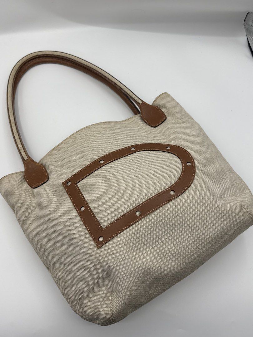 Delvaux (Category: Tote Bags) located in Caloocan City. Submitted by rossvault2 (Listing ID 1465230178, Image 3). Description: - Brand: Delvaux - Material: Beige canvas with brown leather trim and handles - Design: Classic tote style featuring a prominent 'D' logo on the front - Interior: Spacious main compartment with zip closure and patterned lining - Condition: Pre-loved, well-maintained and ready to use.