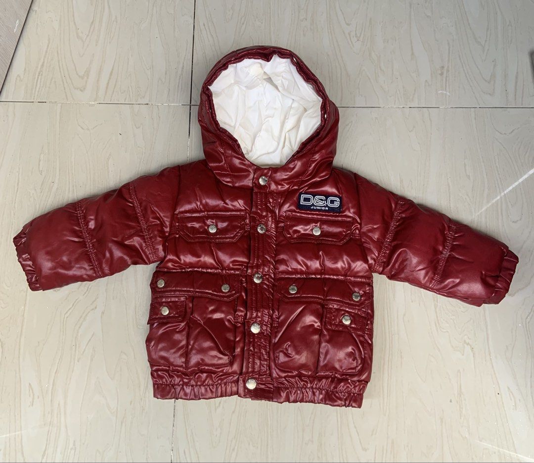 D&G Junior Red Puffer Jacket 6-9 Months (Category: Babies & Kids Fashion) located in Angeles City. Submitted by manlapidma26771 (Listing ID 1465221865, Image 1). Description: - Brand: D&G Junior - Item: Red shiny puffer jacket with hood - Size: 6-9 mesi / 68-74 cm / 26-29 inches - Details: White interior lining, multiple front pockets with silver-toned branded snap buttons, D&G Junior chest logo patch - Condition: Excellent warm winter outerwear 