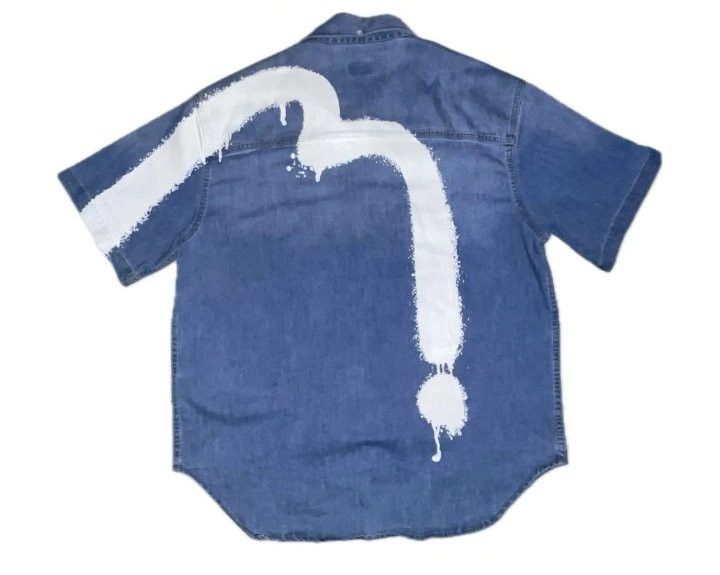 Evisu Daicock Denim Short Sleeve Shirt (Category: Tshirts & Polo Shirts ) located in Puerto Princesa. Submitted by gaspari5300 (Listing ID 1465340771, Image 2). Description: - Brand: Evisu - Style: Short sleeve blue denim shirt with button-down front and pointed collar - Details: Chest pocket featuring a white printed box graphic and small patch accents - Back Design: Signature large white painted Evisu seagull motif across the shoulders - Fit: C