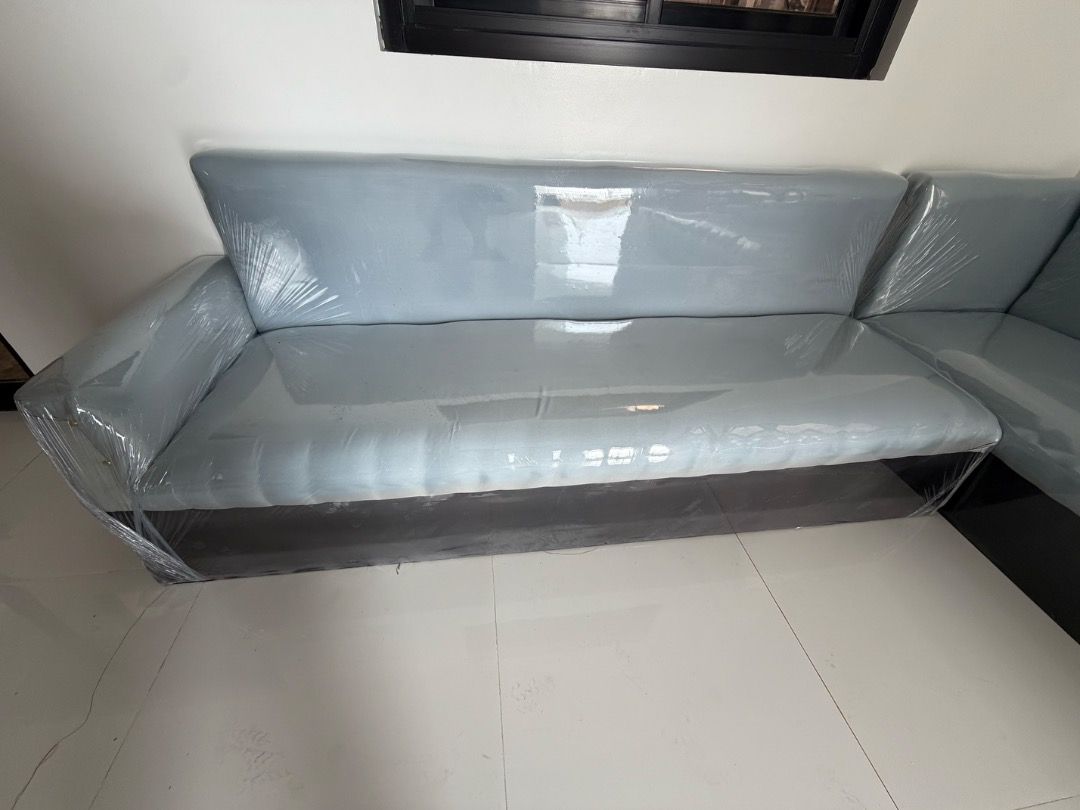 Grey L-shape sectional sofa with matching footstool and throw pillows (Category: Sofas) located in Manila. Submitted by thislivsnjutare (Listing ID 1465285413, Image 2). Description: - Large grey L-shape sectional sofa with a dark grey base and light grey upholstery - Brand new and untouched, still wrapped in protective plastic film - Includes matching throw pillows and a separate footstool ottoman - Space-saving design that fits nicely into livi