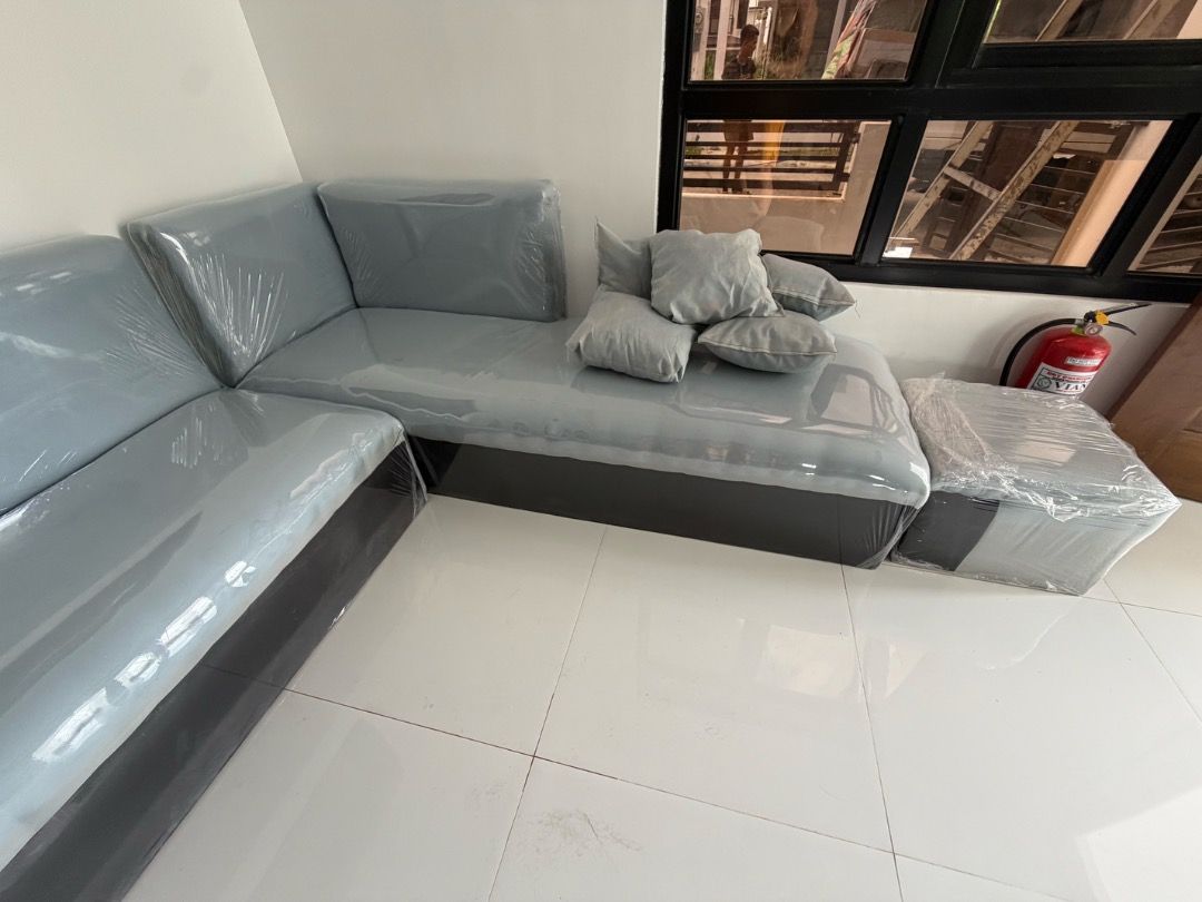 Grey L-shape sectional sofa with matching footstool and throw pillows (Category: Sofas) located in Manila. Submitted by thislivsnjutare (Listing ID 1465285413, Image 3). Description: - Large grey L-shape sectional sofa with a dark grey base and light grey upholstery - Brand new and untouched, still wrapped in protective plastic film - Includes matching throw pillows and a separate footstool ottoman - Space-saving design that fits nicely into livi