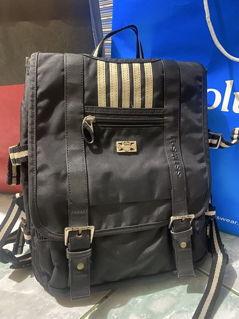 K-Swiss Black Backpack with Striped Details (Category: Backpacks) located in San Narciso. Submitted by boypablo1998 (Listing ID 1465294432, Image 1). Description: - Brand: K-Swiss - Color: Classic Black - Design: Vertical stripes on the front flap and straps with a metal logo badge - Storage: Zippered front pocket and secure main compartment with dual buckle straps - Details: Back straps feature woven K-Swiss text branding with white piping - Fea
