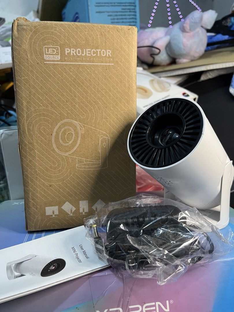LED Source Multimedia Mini Projector with Box and Manual (Category: Projectors) located in Manila. Submitted by abbigail029. (Listing ID 1465200820, Image 1). Description: - Compact white LED multimedia mini projector - Attached adjustable rotating stand for easy positioning - Includes original brown cardboard box - Comes with power adapter in plastic wrapper and user manual - Straightforward setup ideal for portable viewing needs.