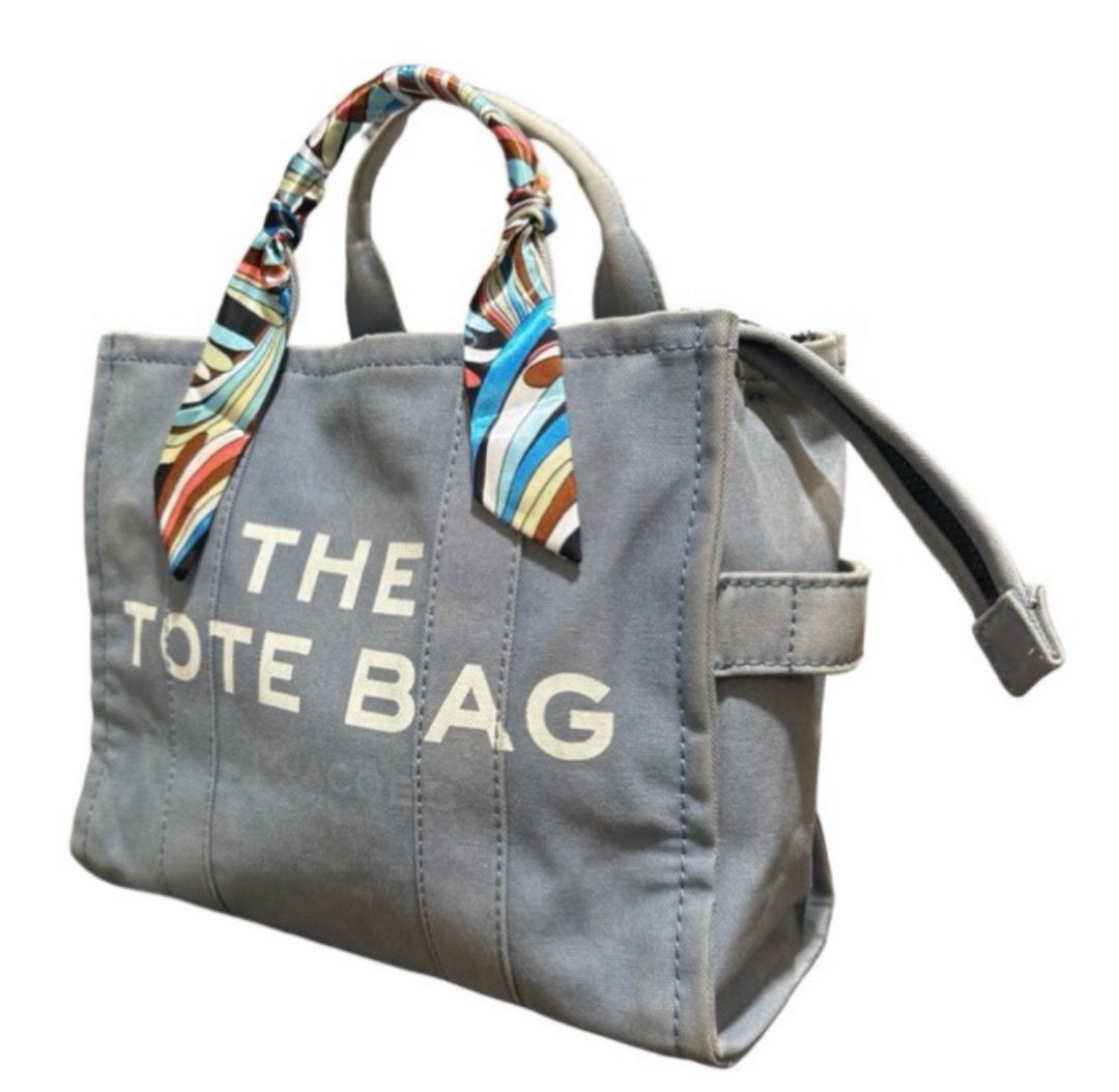 Marc Jacobs The Tote Bag Canvas (Category: Tote Bags) located in Digos. Submitted by tindahannimaria (Listing ID 1465268182, Image 1). Description: - Brand: Marc Jacobs - Color: Light Blue - Includes: Printed ribbon scarf tied on handle - Closure: Secure top zipper - Storage: Convenient interior pockets - Condition: Shows normal signs of use, including handle wear/fraying and uneven, faded fabric coloring - Size: Spacious enough for everyday esse