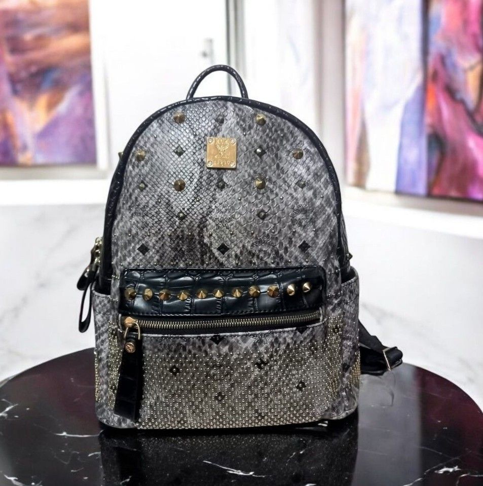 MCM Stark Studded Python Print Backpack (Category: Bags & Wallets) located in Semporna. Submitted by ummicollectionbundle (Listing ID 1465296379, Image 1). Description: URGENT SALE!!! - Brand: MCM - Design: Grey python print with all-over crystals and studs on front and sides - Accents: Black patent leather on front pocket and gold-tone hardware with iconic MCM logo plate - Features: Secure zipper closure, sturdy top handle, and adjustable should