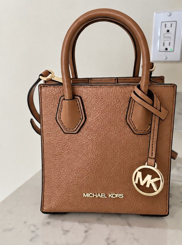 Michael Kors Mercer XS (Category: Luxury Bags & Wallets) located in Manila. Submitted by leluxe1214 (Listing ID 1465180777, Image 1). Description: - Brand: Michael Kors - Color: Brown - Material: Textured finish with gold-tone hardware - Style: Mini tote bag (includes dual top handles and a matching crossbody strap) - Features: Signature hanging MK charm, secure magnetic snap closure, and interior slip pocket - Condition: Excellent / Well-maintai