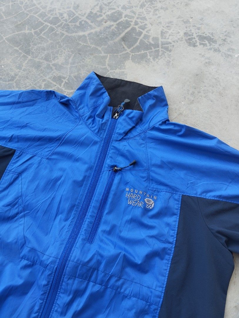 Mountain Hardwear Blue Windbreaker Jacket Size M (Category: Coats, Jackets and Outerwear) located in Mati. Submitted by old_era.ph (Listing ID 1465171782, Image 2). Description: - Brand: Mountain Hardwear - Size: M (Fits true to size) - Color: Bright blue and dark navy panels with black lining - Features: Stand collar, embroidered logos on chest and shoulder, vertical chest pocket, two zippered hand pockets, and adjustable drawstring hem - Origin