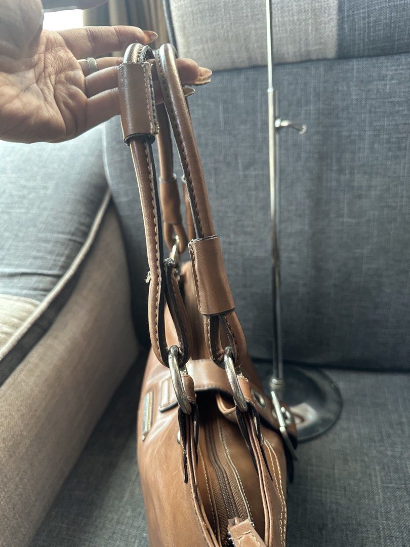 Nine West Brown Shoulder Bag with Tassel (Category: Shoulder Bags) located in Manila. Submitted by goldenhorse-dafc (Listing ID 1465376100, Image 2). Description: - Brand: Nine West - Material: Polyurethane (Brown) - Closure: Zip top - Hardware: Silver-tone - Details: Front buckle and cute hanging tassel - Interior: Fabric-lined with multiple pockets for organization - Flaw: Material peeling on the strap handles (priced accordingly).