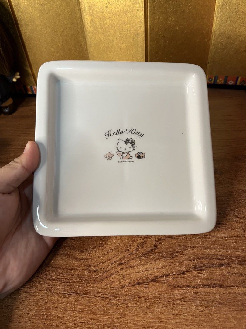 Original Sanrio Hello Kitty Ceramic Square Plate Tray (Category: Dinnerware & Cutlery) located in Gapan. Submitted by lunashop14 (Listing ID 1465175945, Image 1). Description: - Authentic Sanrio Kitty white ceramic square plate - Features a charming Kitty graphic with teacup and gift box illustrations - Dated '76, '05 Sanrio copyright near the bottom - Raised rim design with an indented cross pattern underneath - Finished with a smooth, glossy gl