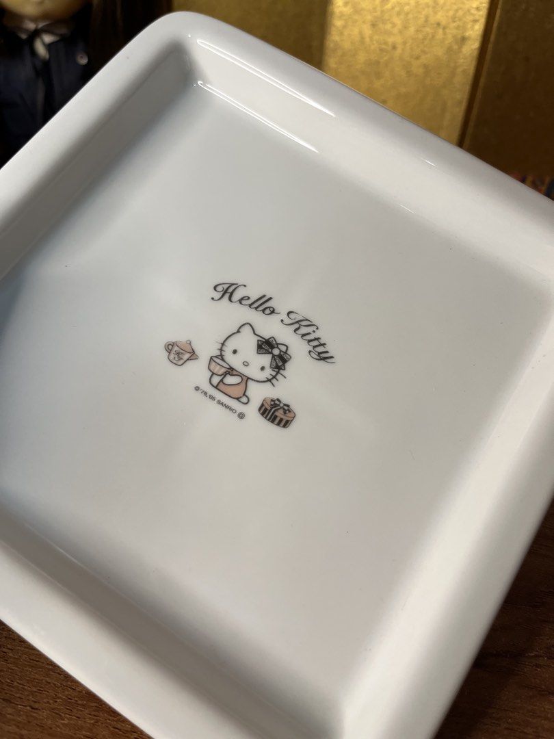 Original Sanrio Hello Kitty Ceramic Square Plate Tray (Category: Dinnerware & Cutlery) located in Gapan. Submitted by lunashop14 (Listing ID 1465175945, Image 3). Description: - Authentic Sanrio Kitty white ceramic square plate - Features a charming Kitty graphic with teacup and gift box illustrations - Dated '76, '05 Sanrio copyright near the bottom - Raised rim design with an indented cross pattern underneath - Finished with a smooth, glossy gl