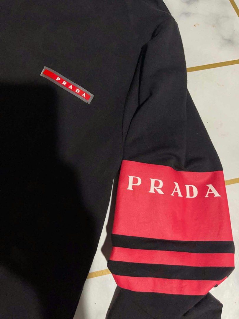 Prada Milano Black Long Sleeve Turtleneck Size M (Category: Longsleeves) located in Manila. Submitted by fastforest_65f95b (Listing ID 1465184507, Image 2). Description: - Brand: Prada Milano - Item: Long sleeve turtleneck shirt - Color: Black with red accents - Size: Medium - Material: Soft, comfortable cotton - Details: Red & black striped band with bold Prada lettering on left sleeve, matching red Prada logo badge on chest - Style: Classic hig