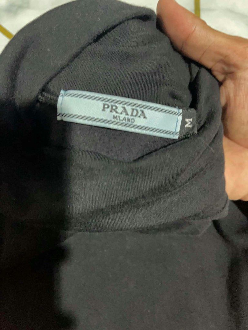 Prada Milano Black Long Sleeve Turtleneck Size M (Category: Longsleeves) located in Manila. Submitted by fastforest_65f95b (Listing ID 1465184507, Image 3). Description: - Brand: Prada Milano - Item: Long sleeve turtleneck shirt - Color: Black with red accents - Size: Medium - Material: Soft, comfortable cotton - Details: Red & black striped band with bold Prada lettering on left sleeve, matching red Prada logo badge on chest - Style: Classic hig