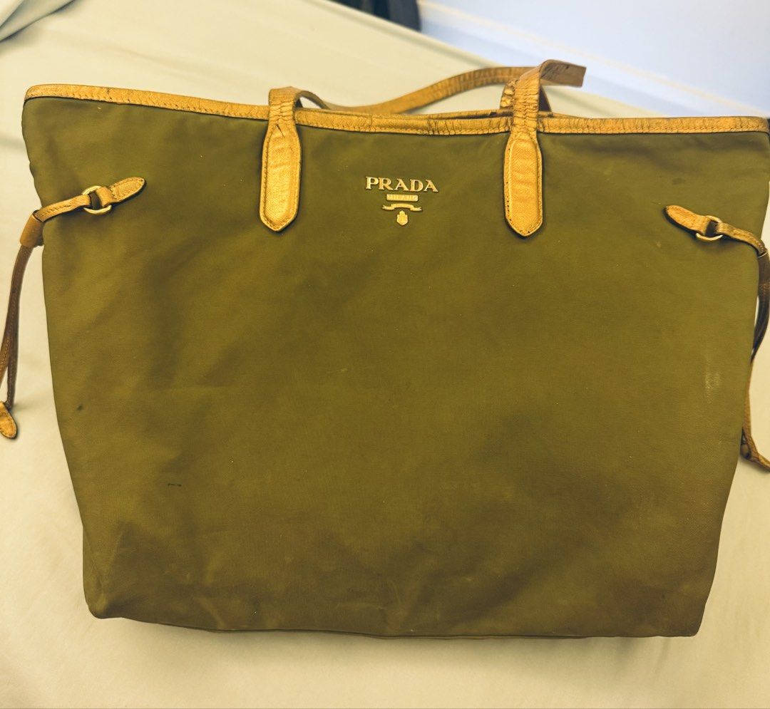 Prada Nylon Khaki Tote Bag (Authentic but restored) (Category: Tote Bags) located in Santa Rosa. Submitted by declutteredbyanna (Listing ID 1465214583, Image 1). Description: Authentic Prada tote bag - but the handle was restored to a gold handle (you can check the last pic for how it looked like before restoring) Bag needs cleaning and flaws shown in pictures so I’m selling it low Price still negotiable :) pm your offer.